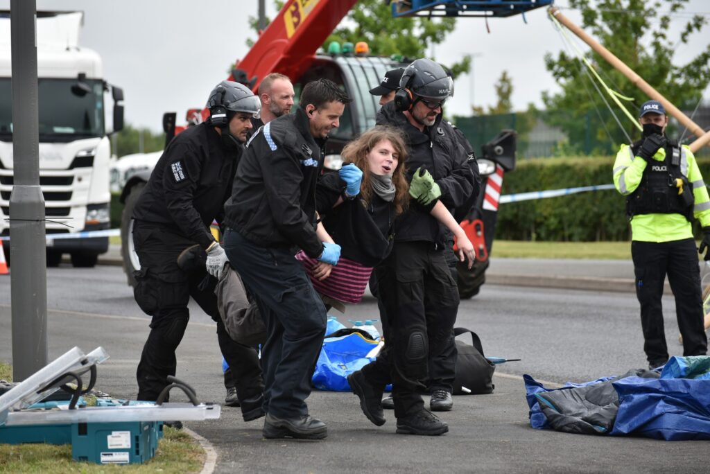 A protester being taken away by four police officers outside Arla HQ