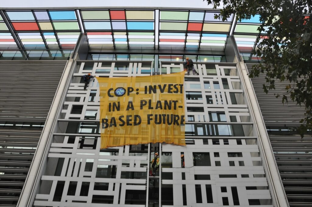 Two climbers hold a banner which states "COP26: invest in a plant-based future" on the wall of DEFFRA