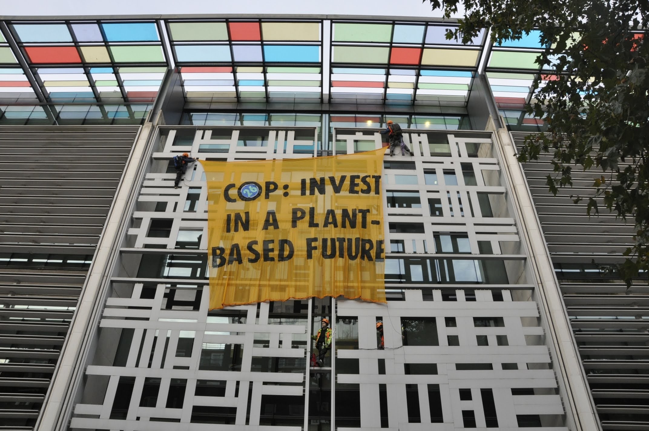 Two climbers hold a banner which states "COP26: invest in a plant-based future" on the wall of DEFFRA