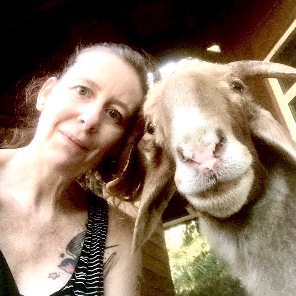 Photo of Nunu Salla indoors with a goat, both looking into the camera lens close-up