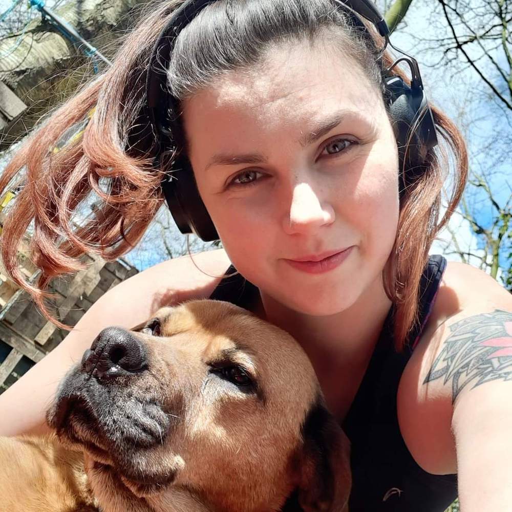 A photo of Summer wearing headphones hugging her dog in the sunshine