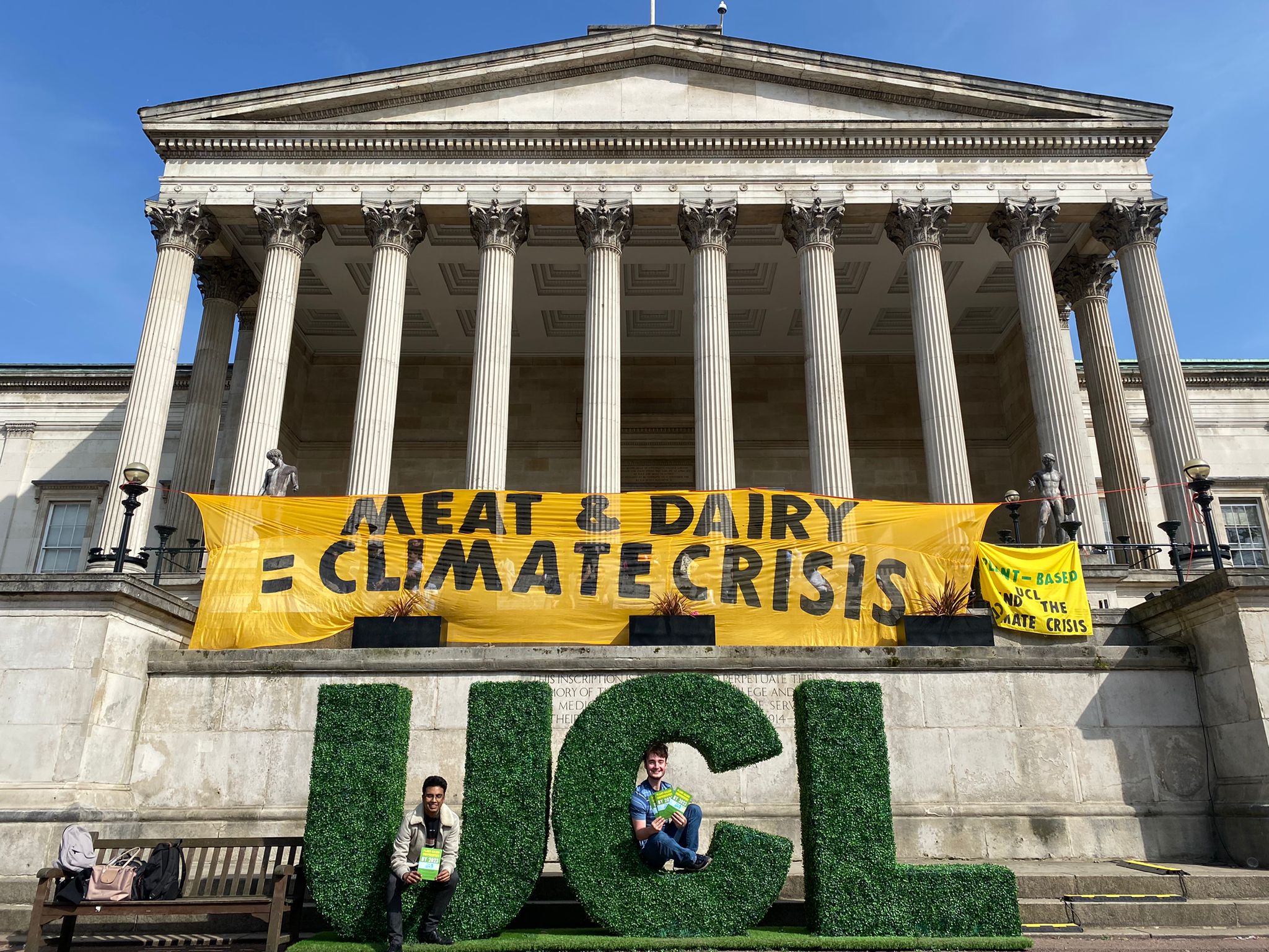 Photo of protesters at UCL displaying a yellow banner with black text reading 'Meat & dairy = climate crisis'