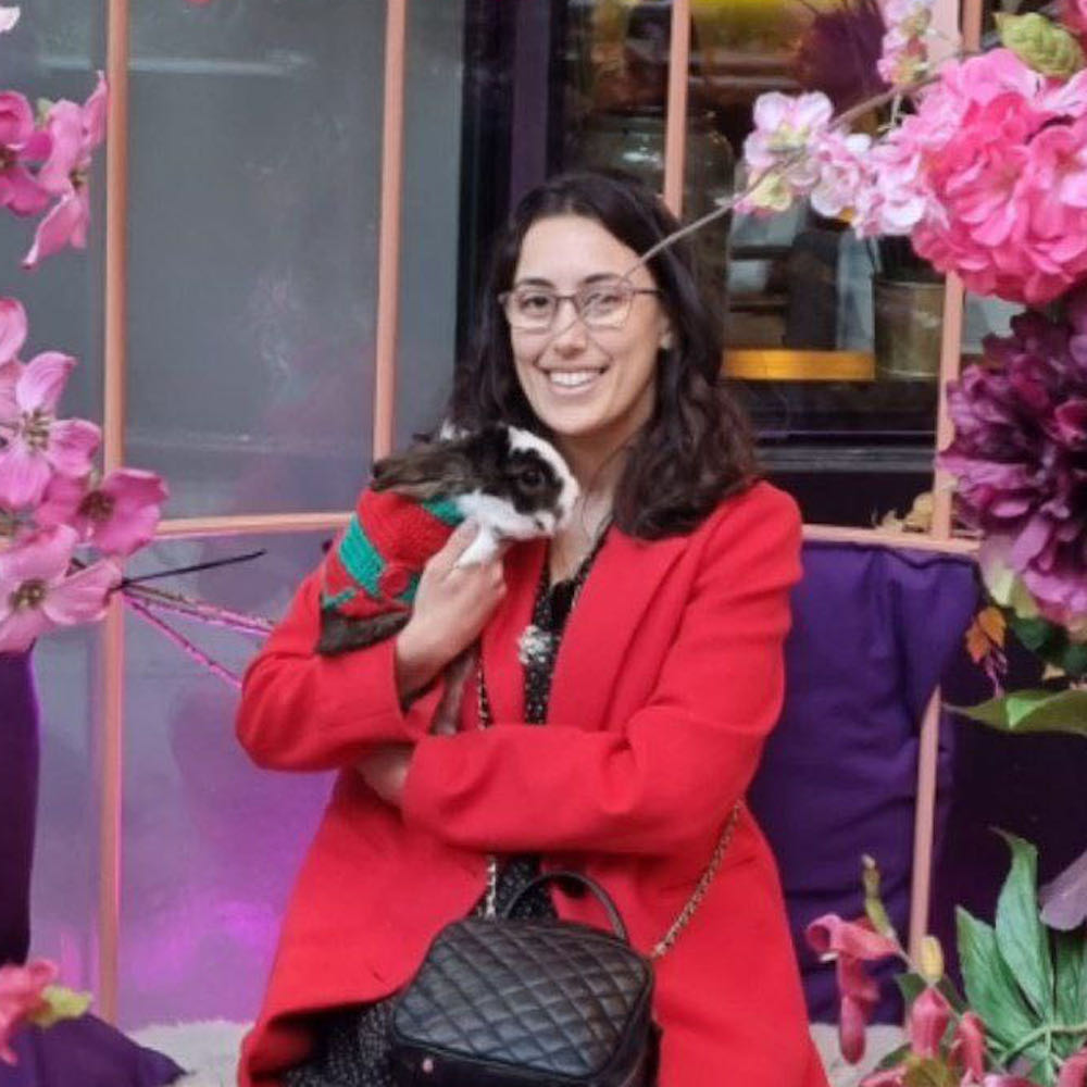 Photo of Sofia sitting amongst pink flowers and smiling whilst holding a rabbit